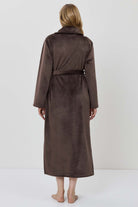 A woman wearing a long brown plush bathrobe with a tie belt.