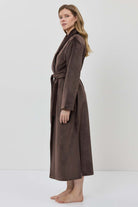 A woman wearing a long brown plush bathrobe with a tie belt.