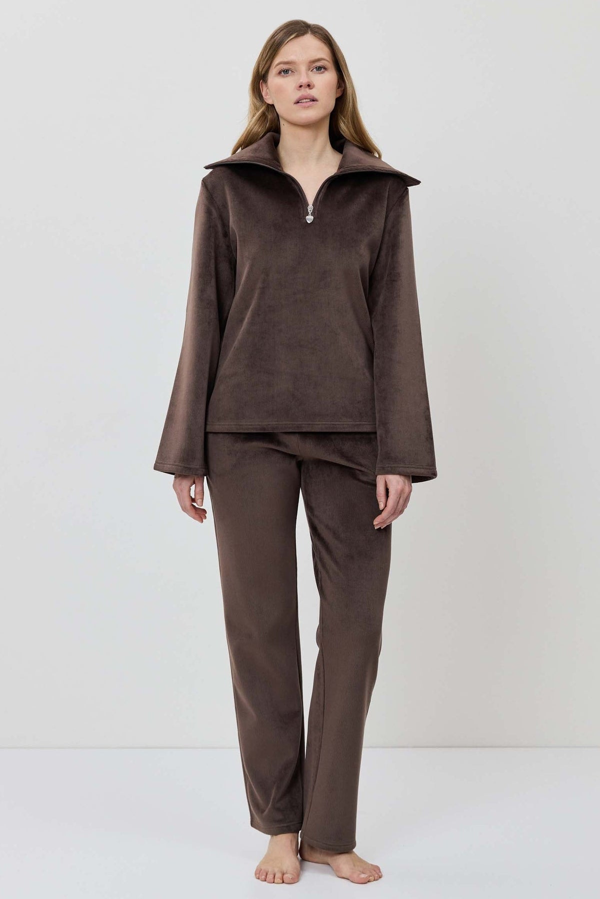 A woman modeling a matching two-piece lounge set in dark brown, featuring a long-sleeve half-zip pullover and coordinating pants.