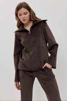 A woman modeling a matching two-piece lounge set in dark brown, featuring a long-sleeve half-zip pullover and coordinating pants.