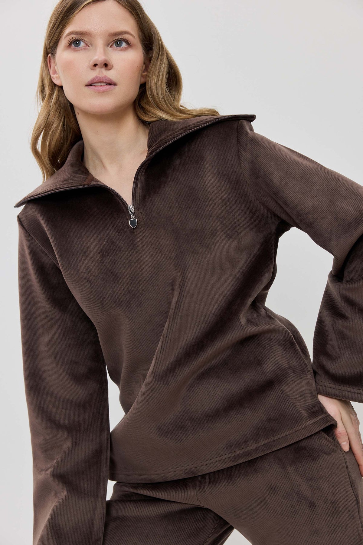 A woman modeling a matching two-piece lounge set in dark brown, featuring a long-sleeve half-zip pullover and coordinating pants.