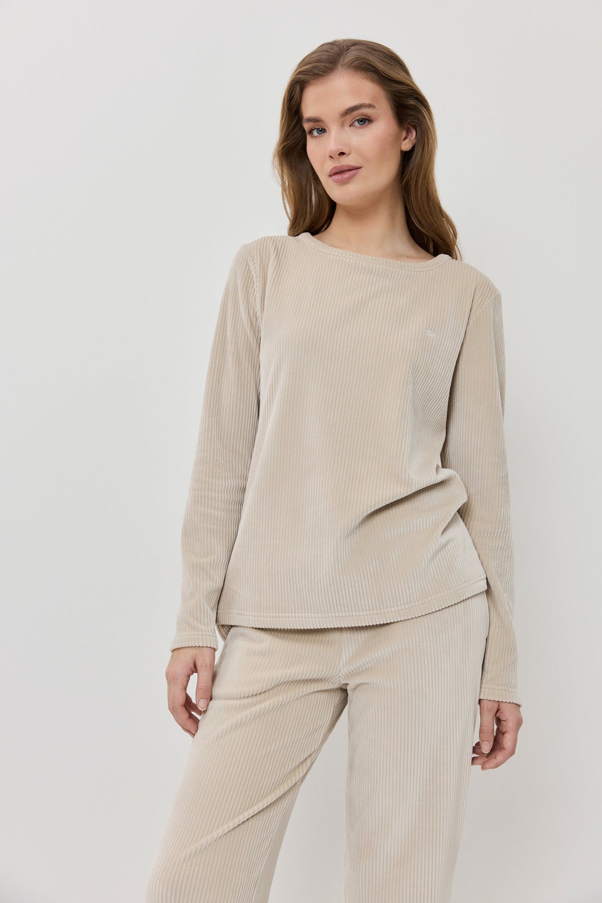 Woman wearing a beige ribbed sweater and pants on a white background