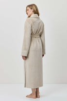 Woman wearing a beige robe standing against a white background