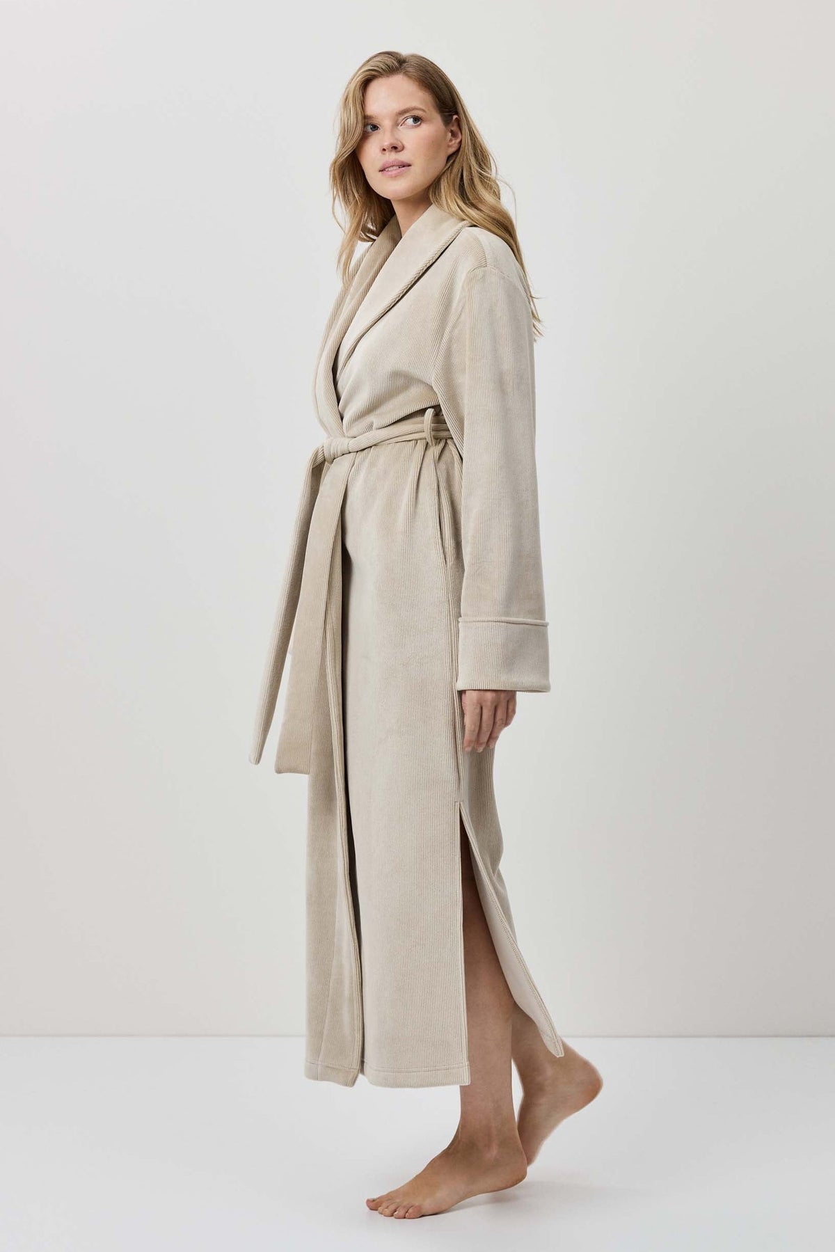Woman wearing a beige robe standing against a white background