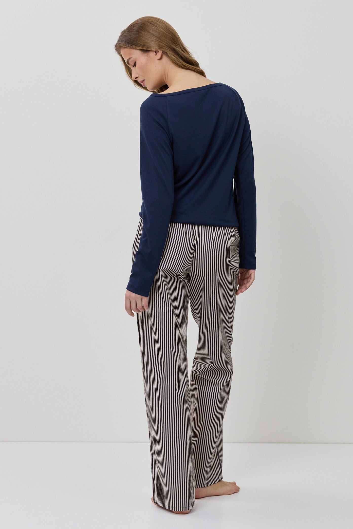 Woman wearing a navy sweater and gray striped pants on a white background