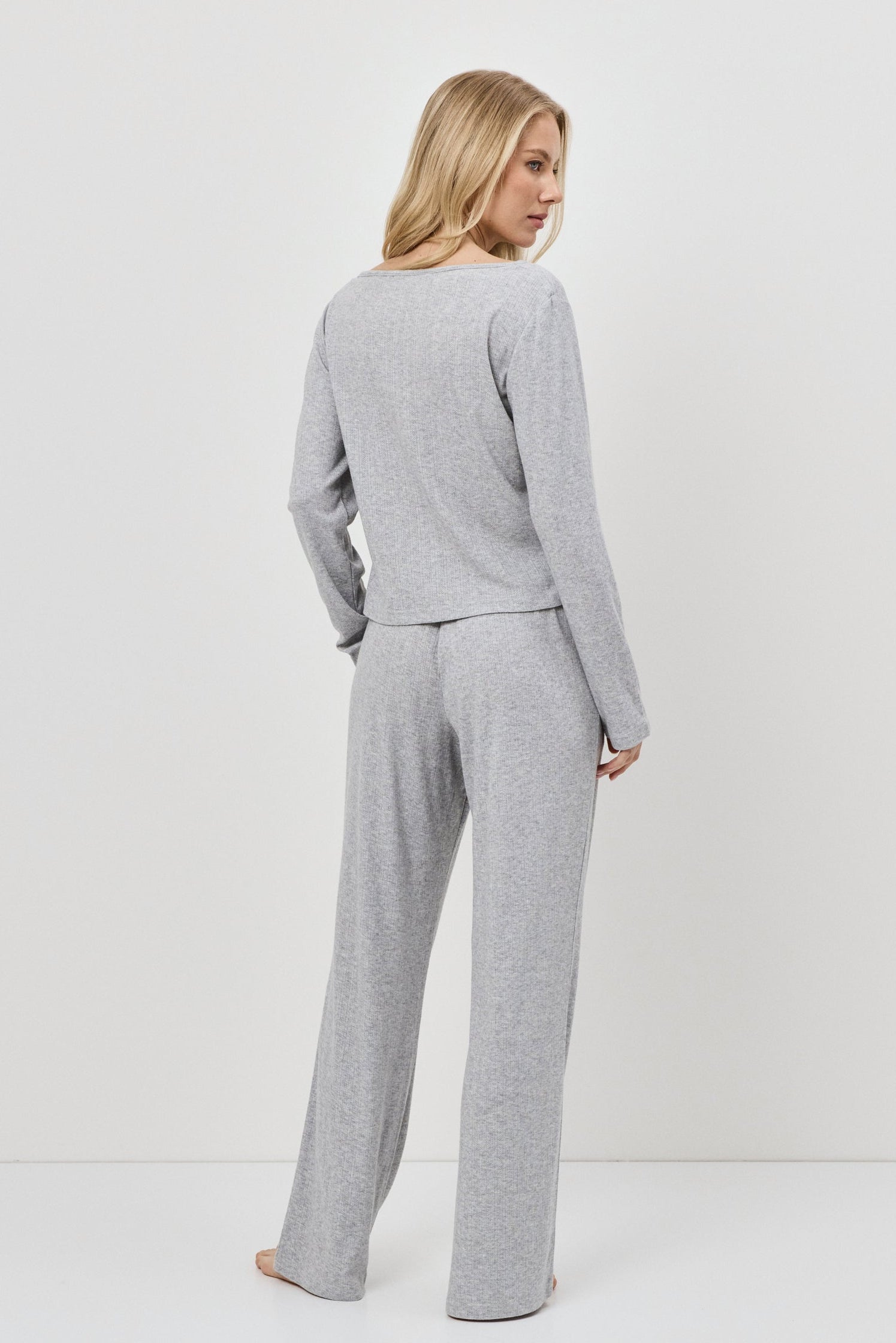 Woman wearing a gray pajama set standing against a white background