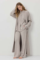 Woman wearing a beige long-sleeve shirt and wide-leg pants against a white background