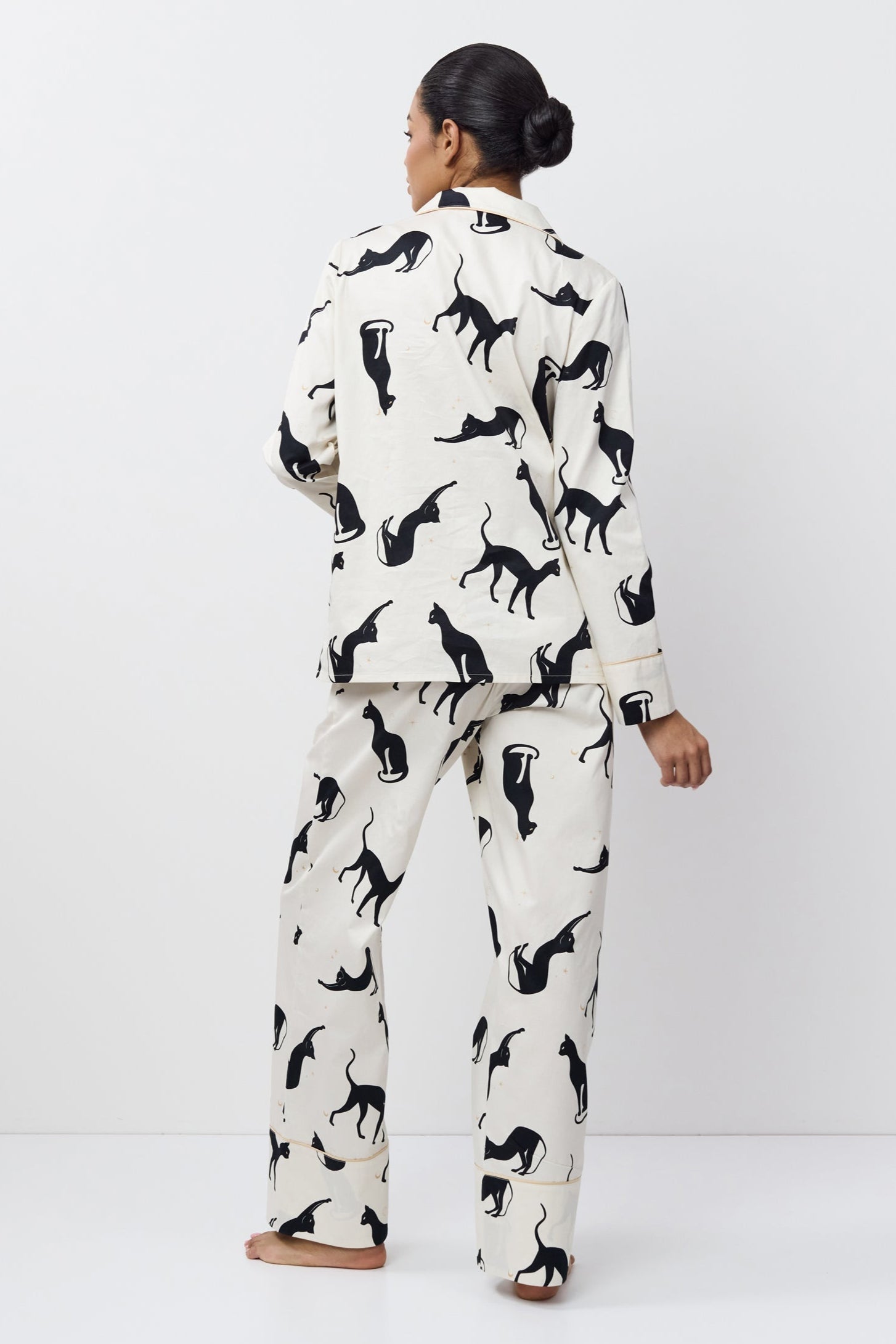 Woman wearing a white pajama set with black cat prints on a white background