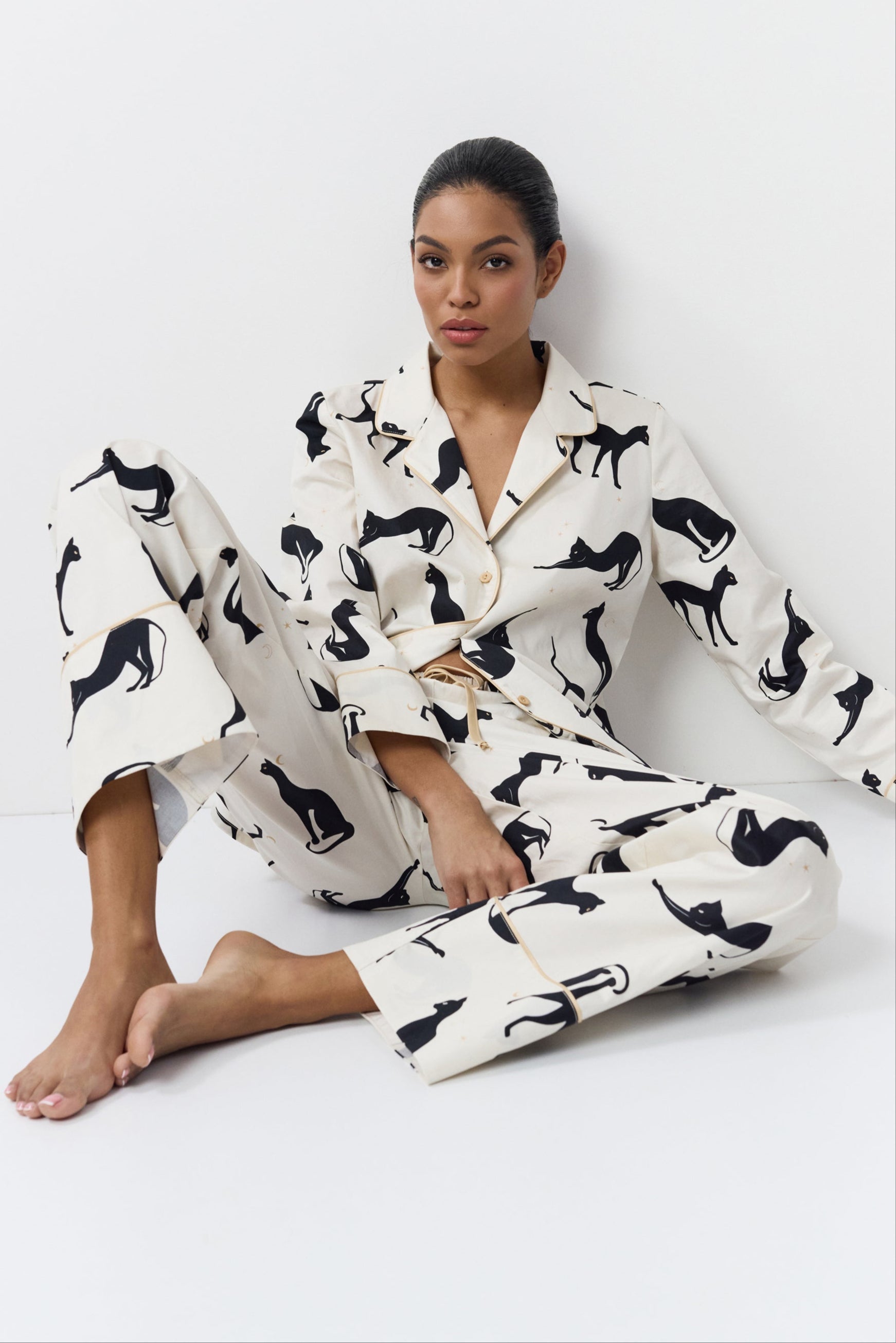 Woman wearing a white pajama set with black cat prints on a white background