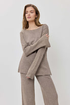 Woman wearing a beige sweater and pants on a light gray background