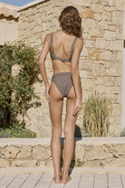 Woman in a bikini standing in front of a stone wall and building.