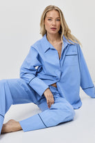 Woman wearing a light blue pajama set sitting on a white surface with a white background