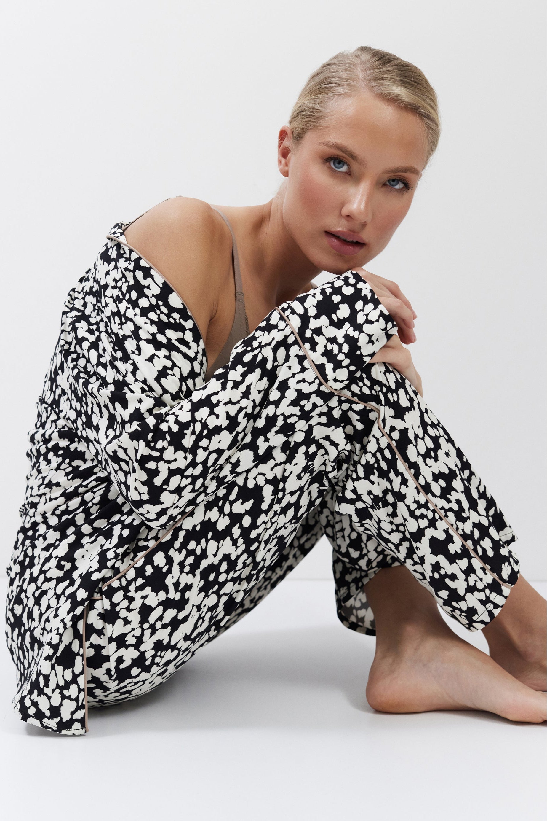 Woman wearing a black and white patterned pajama set sitting on a white background