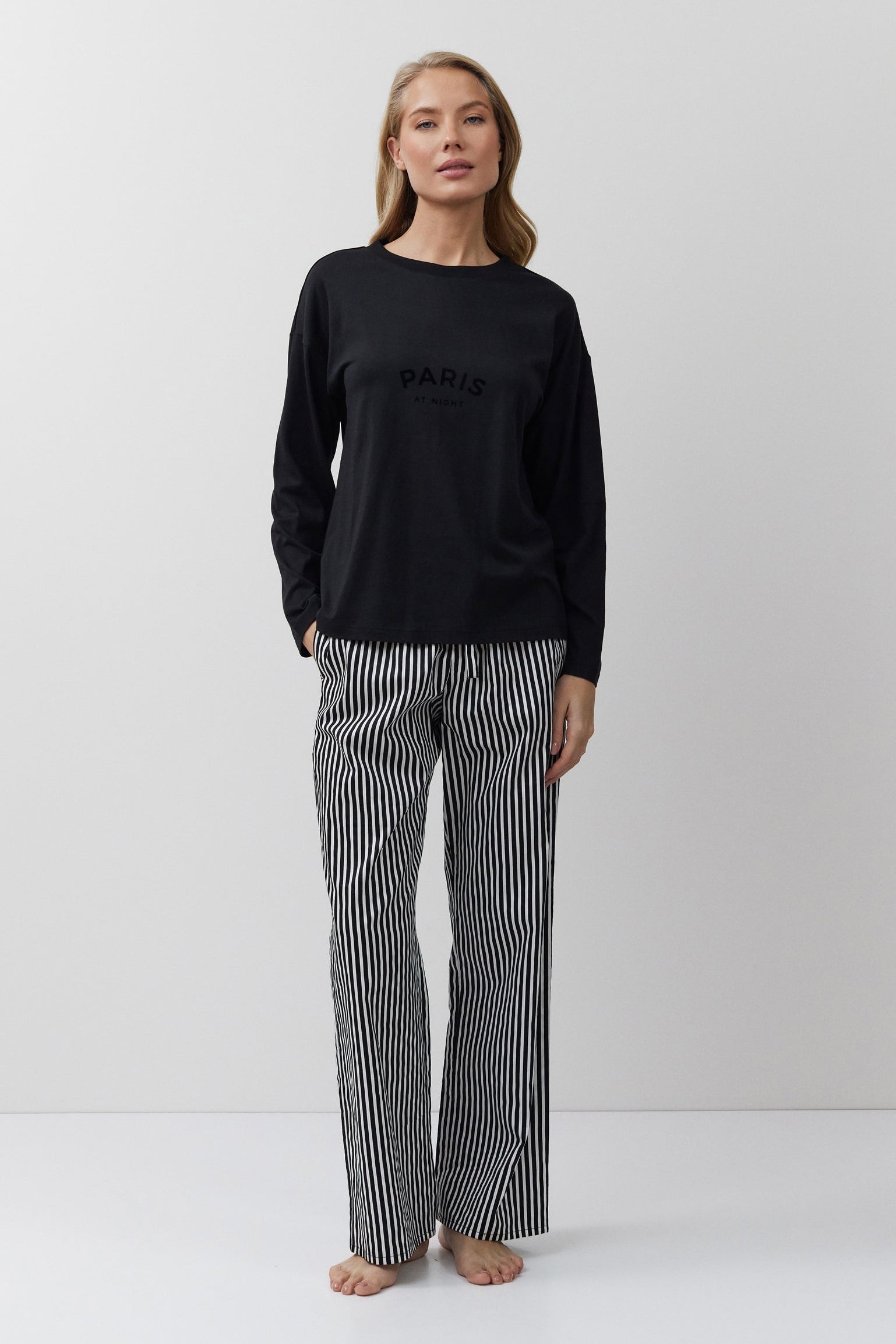 Woman wearing a black long-sleeve top and striped pants on a white background