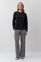 Woman wearing a black long-sleeve top and striped pants on a white background