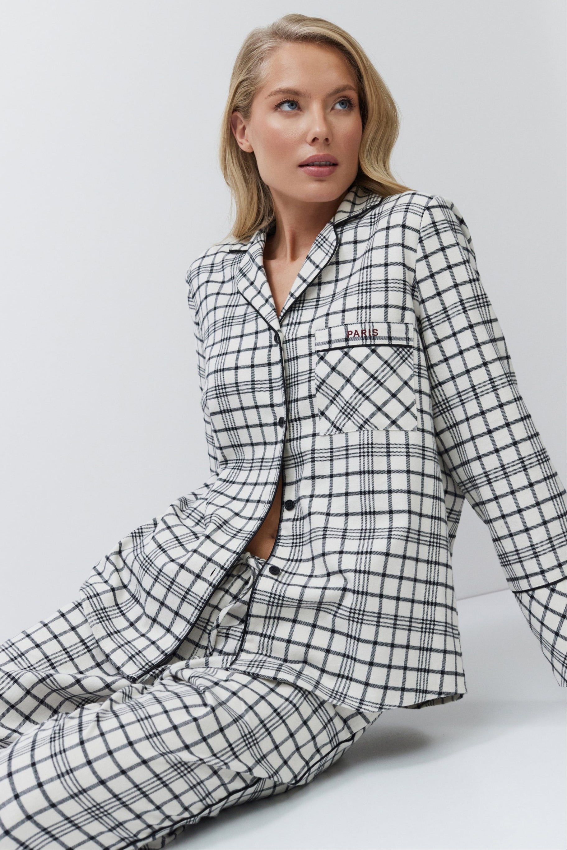 Woman wearing a black and white checkered pajama set sitting on a white background
