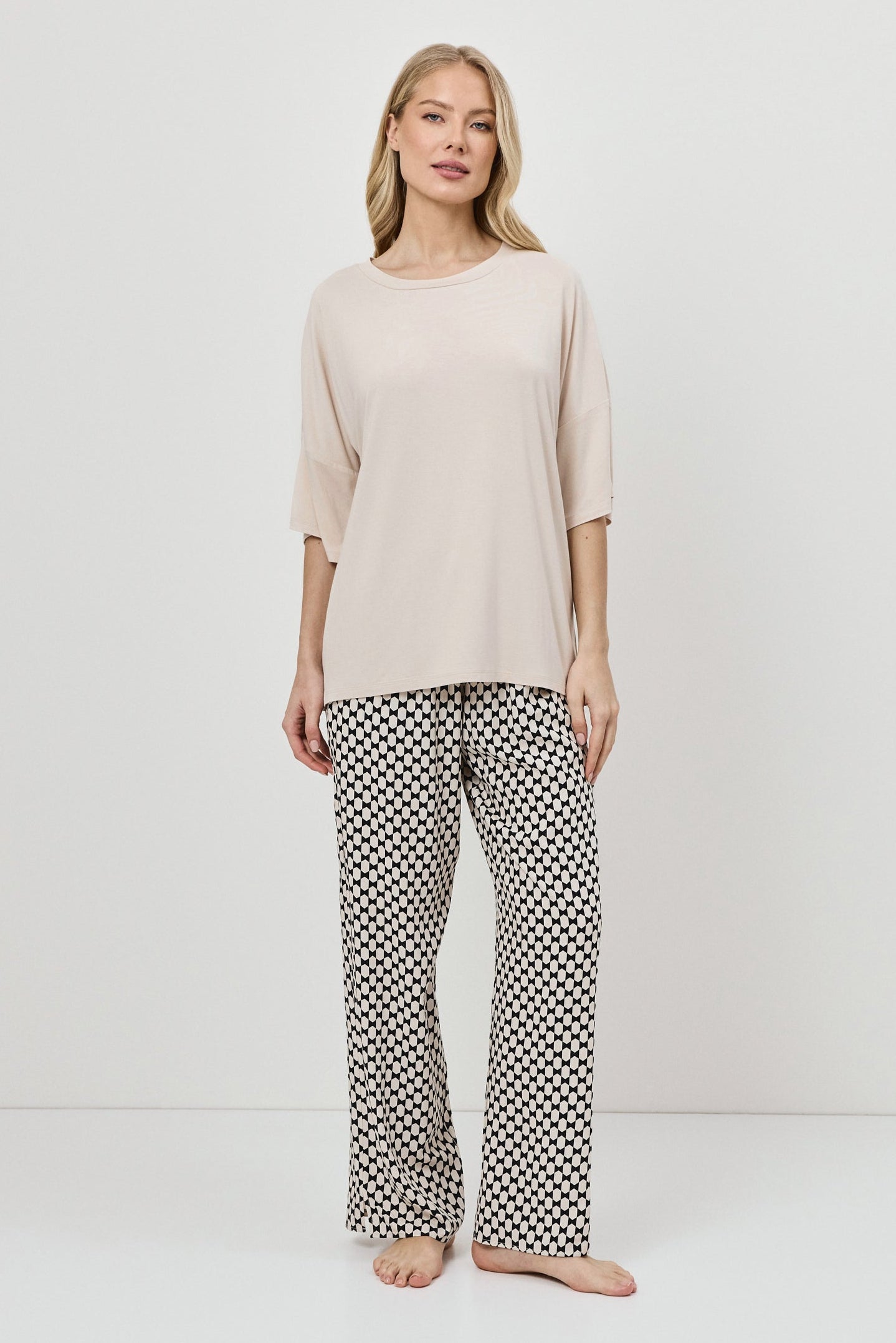 Woman wearing a beige top and patterned pajama pants on a white background