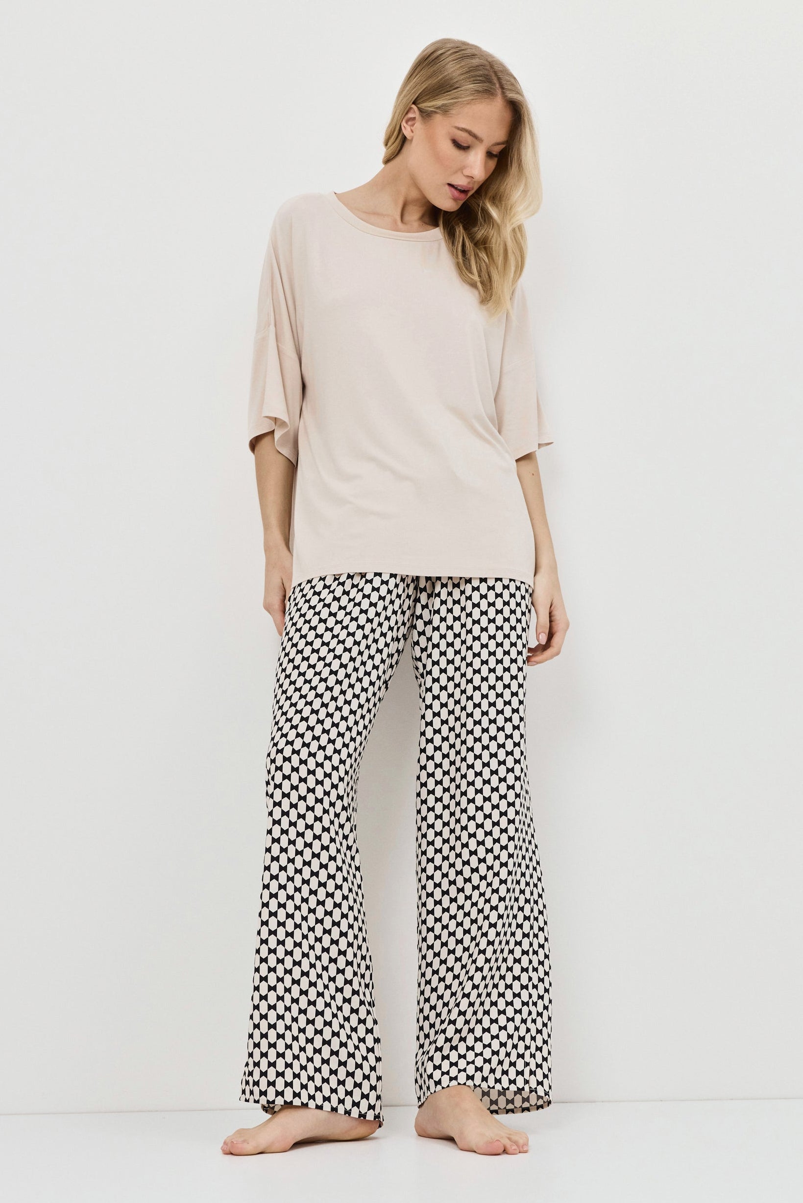 Woman wearing a beige top and patterned pants on a white background
