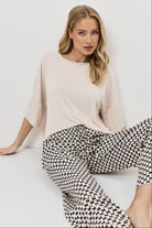 Woman wearing a beige top and patterned pants on a white background