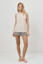Woman wearing a beige sleeveless top and patterned shorts on a white background