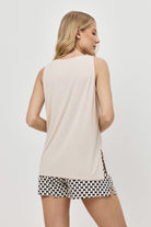 Woman wearing a beige sleeveless top and patternedshorts on a plain background