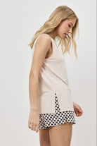 Woman wearing a beige sleeveless top and black and patterned shorts on a plain background